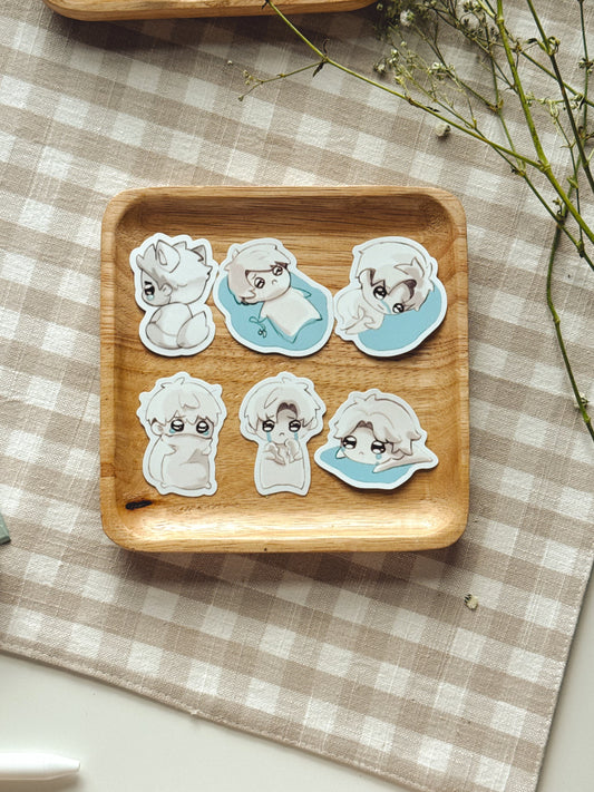 Six love and deepspace love interest chibi stickers displayed on a small wooden tray over a beige-and-white checkered cloth, with dried flowers and part of another tray visible around it.